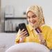 Easy payments. Smiling arabic woman or muslim woman in hijab in headscarf using phone and credit