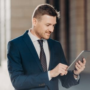 Successful male office worker dressed in elegant suit, holds modern digital tablet, updates website