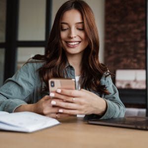 Beautiful smiling woman using cellphone while working with laptop