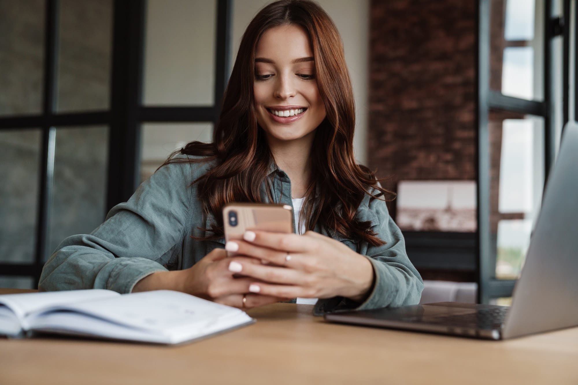 Beautiful smiling woman using cellphone while working with laptop