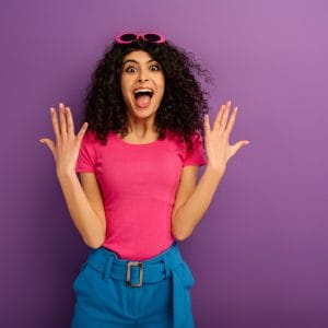 excited bi-racial girl showing wow gesture while looking at camera on purple background