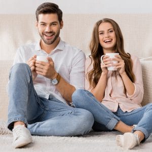 happy loving couple with cups of coffee resting on sofa at home